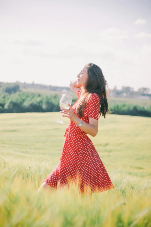 a girl standing in tall grass drinking from a glass