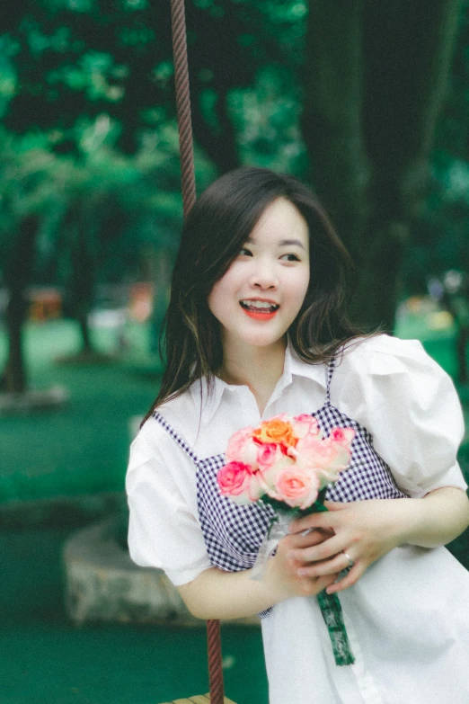 a smiling young woman holding flowers sitting on a swing