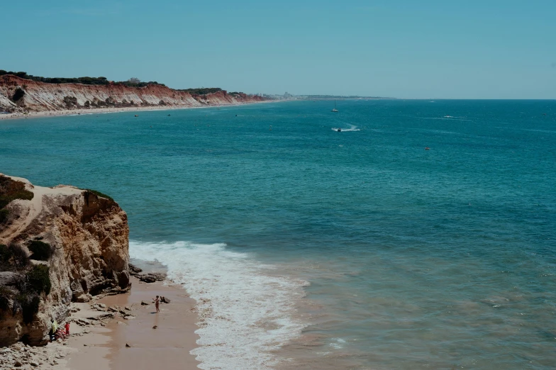 view of a sandy beach with several people in the water and a cliff