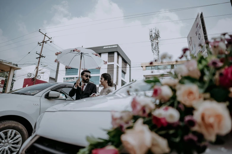 a bride and groom next to a white car with an umbrella