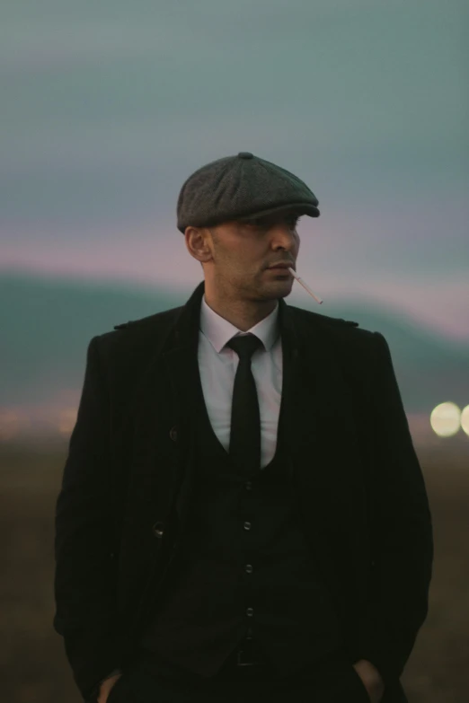 a man wearing a cap, jacket, tie and baseball hat with a sky background