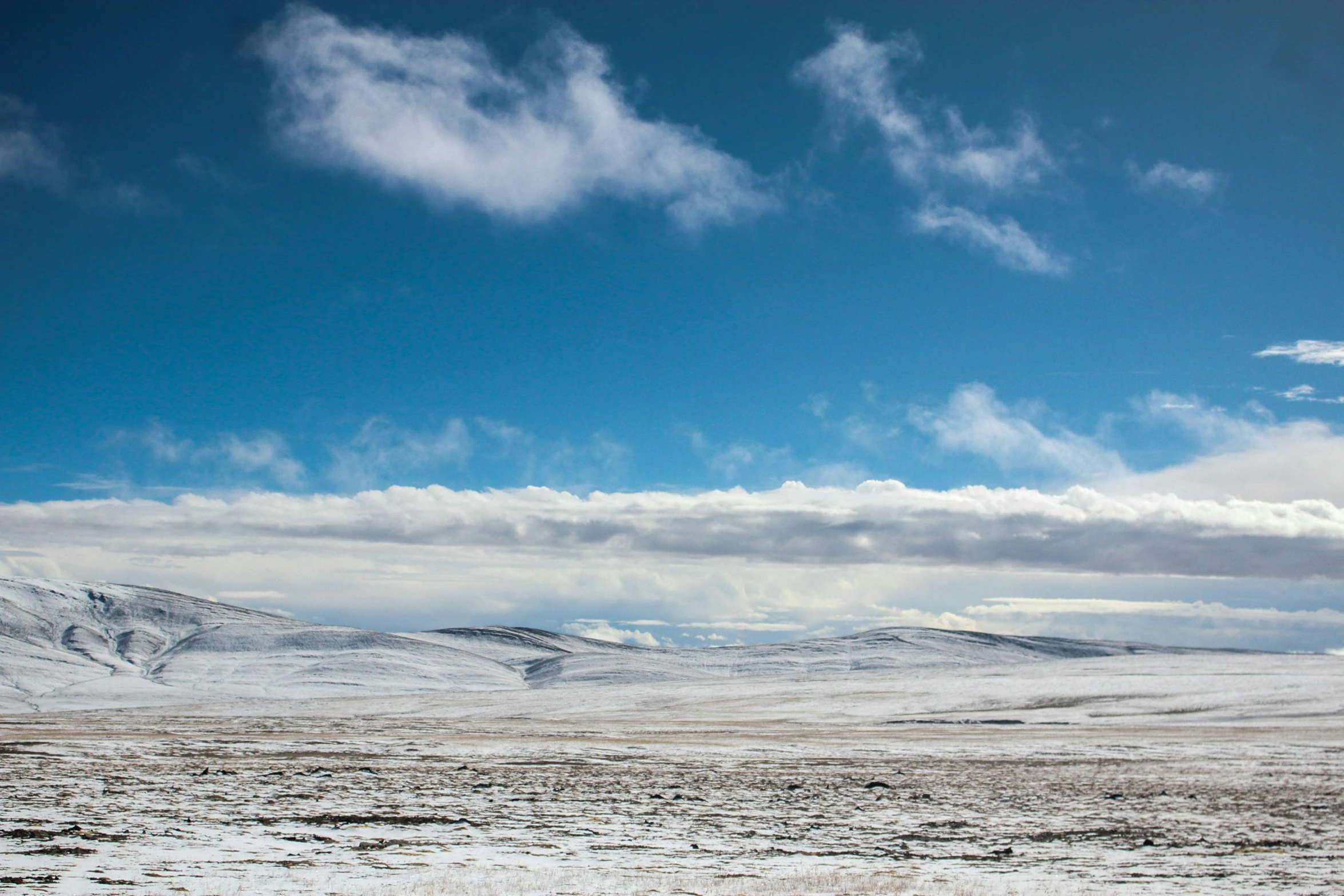 a snowy, flat landscape with mountains and clouds in the background