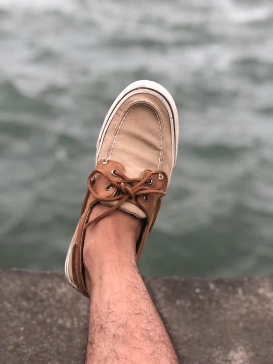 someone wearing a pair of brown shoes, and standing by the water