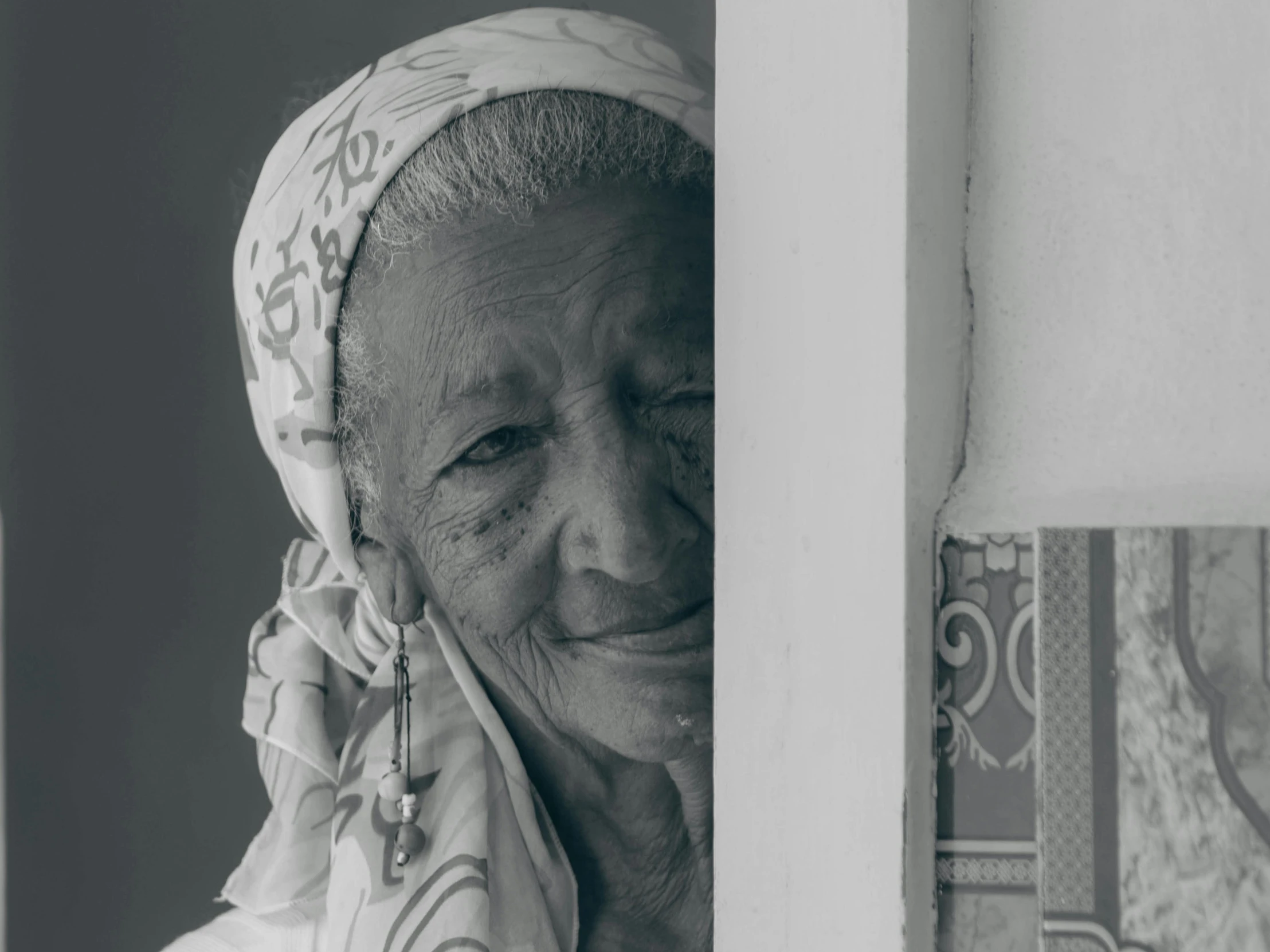 an elderly woman poses for the camera next to a wall