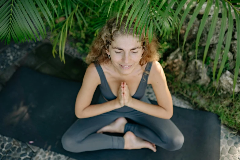 a girl sitting in a lotus position by some plants
