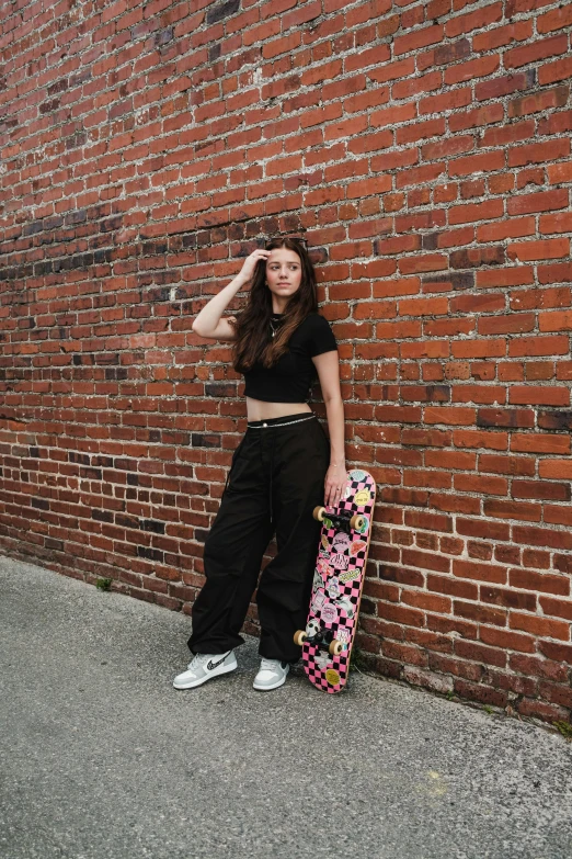 a girl in black sports clothes is leaning against a brick wall with a skateboard