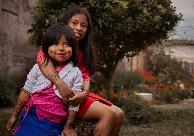 two children sitting in front of a tree wearing red and white makeup