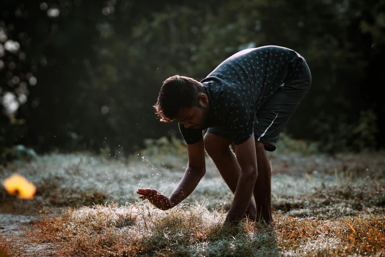 young man kneeling in field using splatter on dry grass