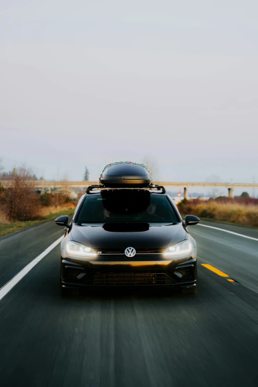 a black volkswagen car traveling on the road with the hood on