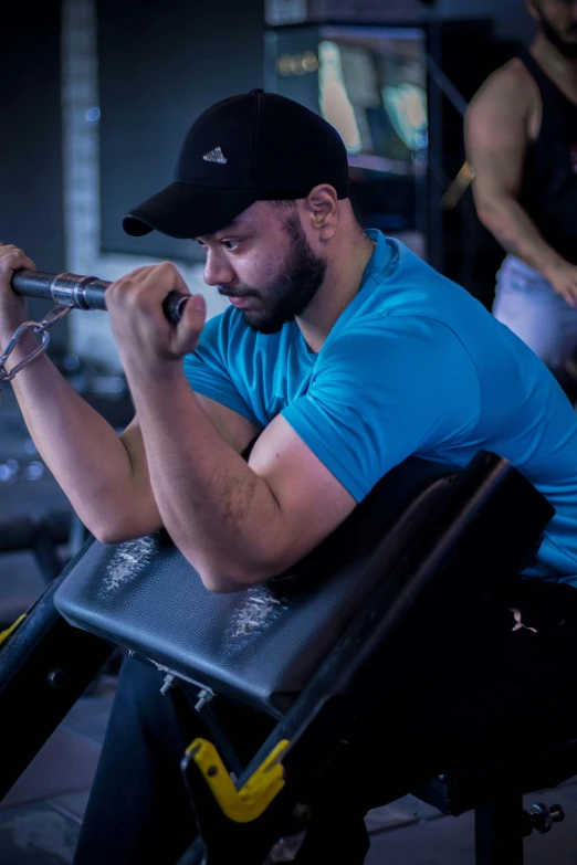 a man wearing blue shirt and cap using equipment at gym