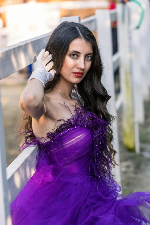 a young woman in a purple dress is leaning against a fence