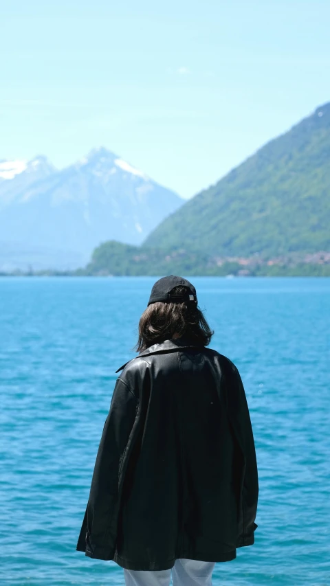 a man with a long hair standing next to a body of water