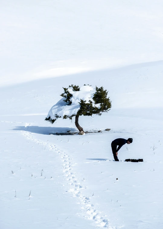 person bent down as their snowboarder kneels down to pick up their footprints