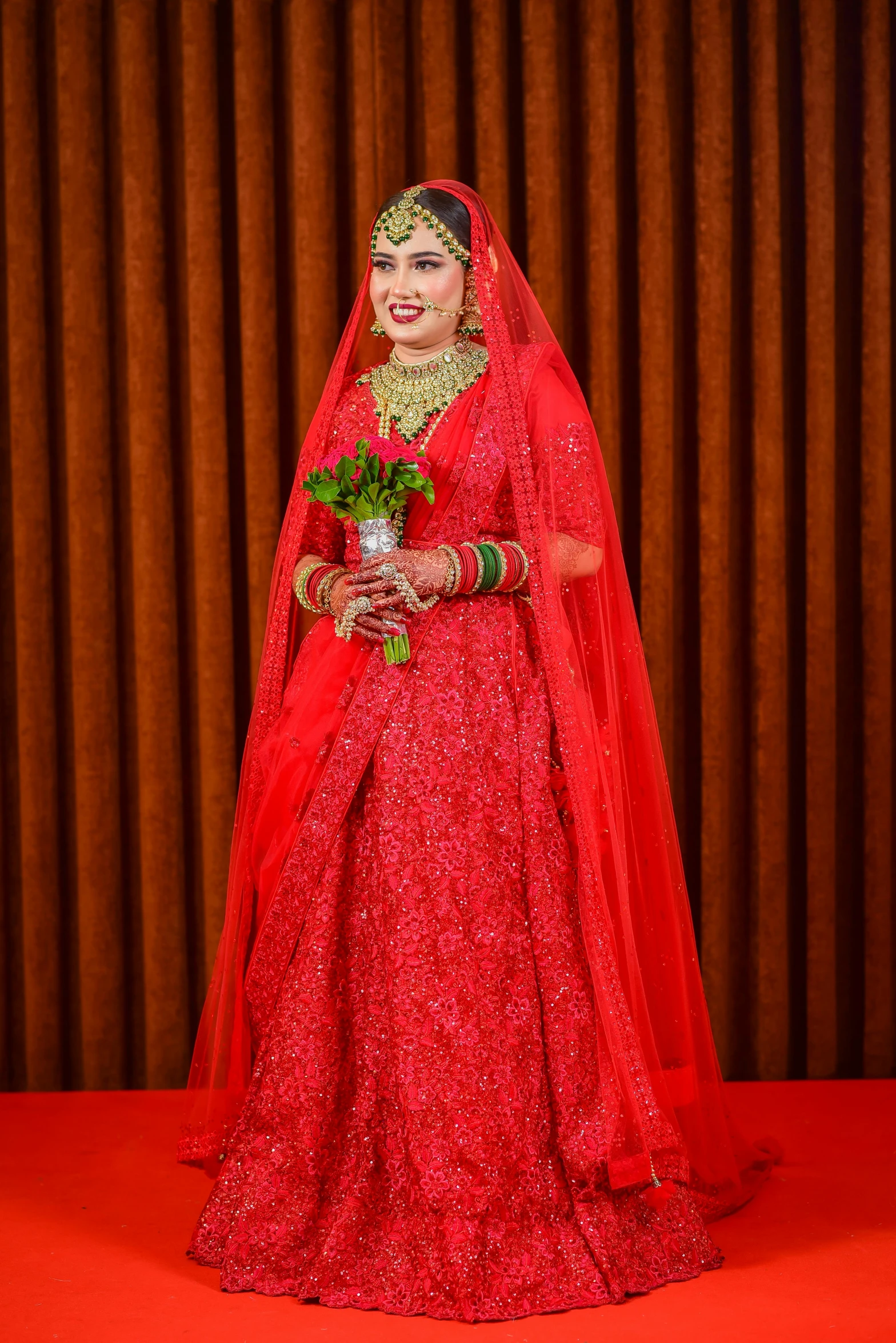 a woman wearing a red dress with gold accessories, a tiara and holding a rose