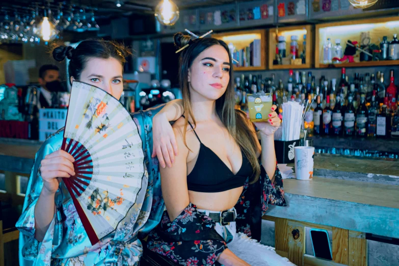 a couple of women holding up paper fans in front of a bar