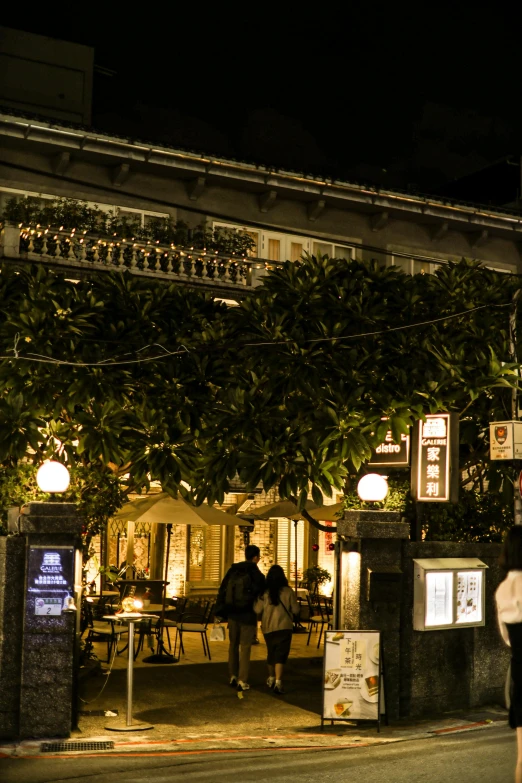 two people standing outside of an outdoor restaurant at night