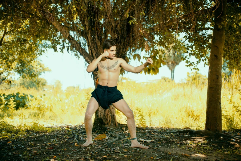 a shirtless man with  is holding a frisbee in front of a tree