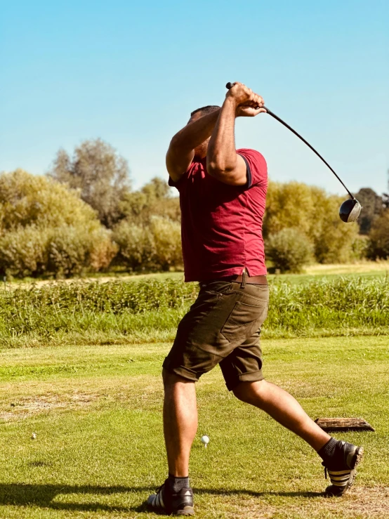 a person in red shirt swinging a golf club