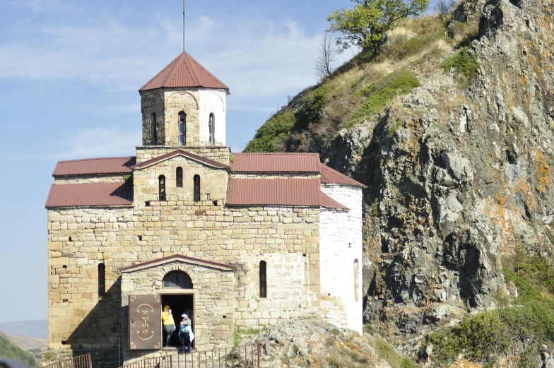 a stone building sits next to a hill with trees on top