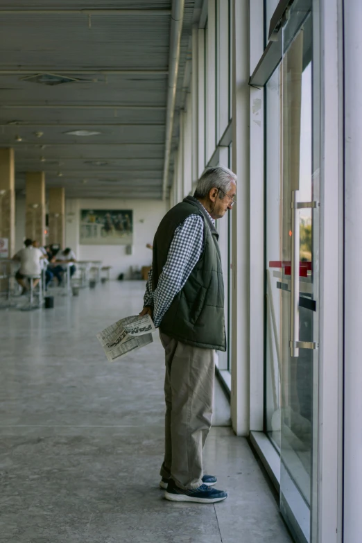 an old man stands by the glass door of a building
