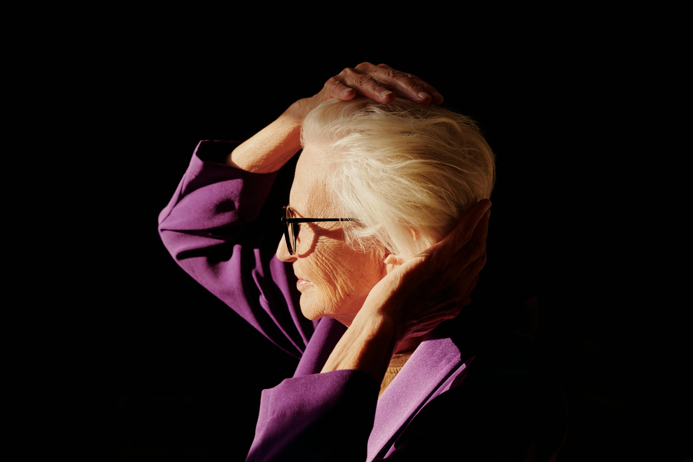 an elderly woman in glasses adjusts her hair