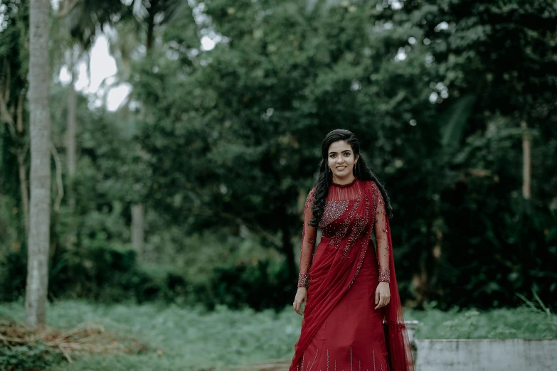 a woman is wearing a red gown and standing in front of trees