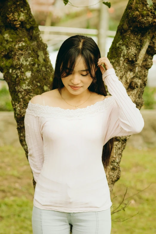 a young woman standing in front of a tree wearing a white top