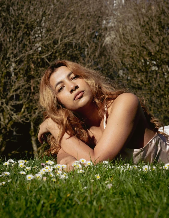 a beautiful young woman laying on top of a green field