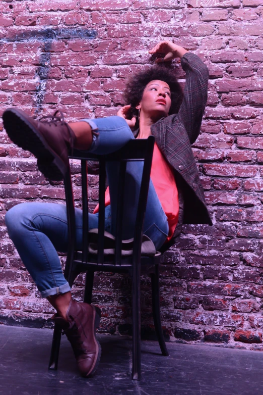 a young woman sits on a chair in front of a brick wall