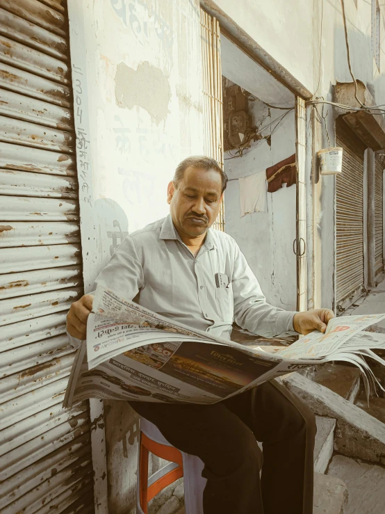 man reading a newspaper while sitting down in front of a building