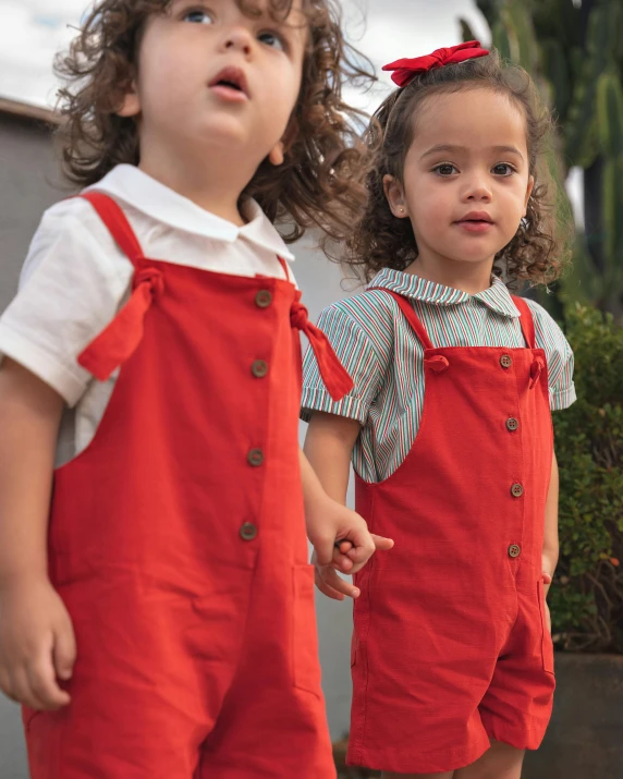 two s wearing red overalls and shorts standing side by side