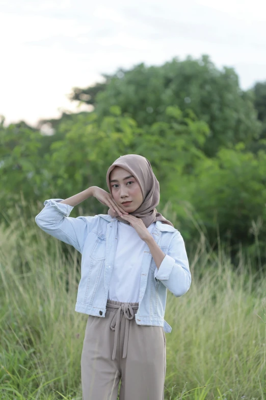 a woman stands in tall grass while wearing a headscarf