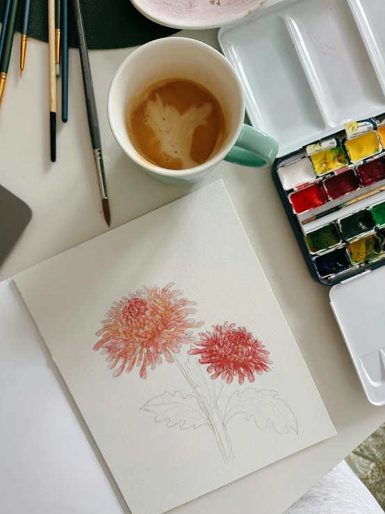 coffee in mug sits next to an open box of paint and watercolor