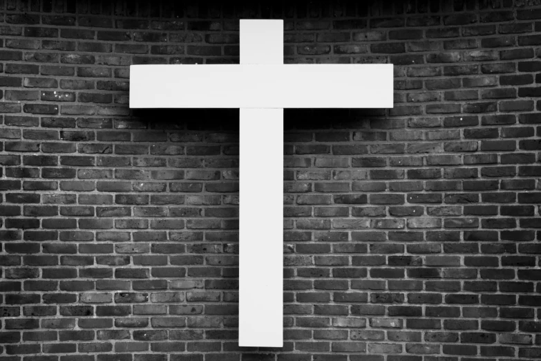 a cross standing against a brick wall on a sidewalk