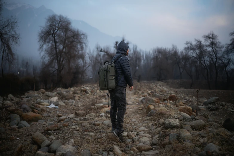 a man is in the woods with his back to the camera, wearing a jacket and backpack