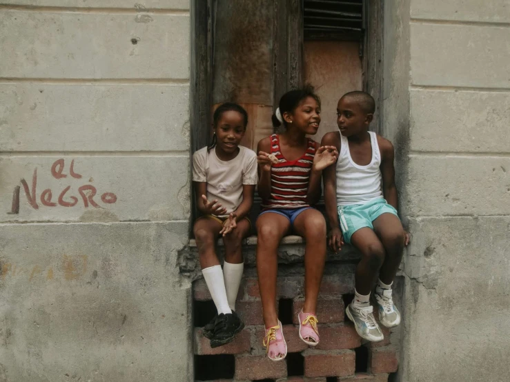 a group of children sitting on a wooden ledge outside a building