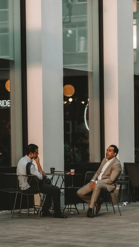 two men sitting outside on chairs talking to each other