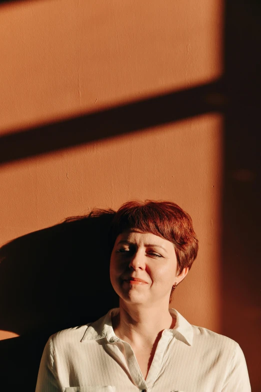 red - headed woman smiling against a brown wall