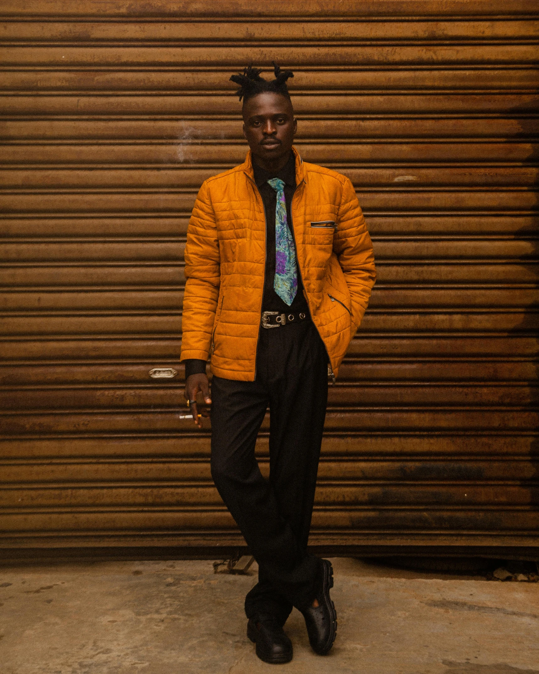 a man in a jacket and tie stands against a wall with his arms behind him