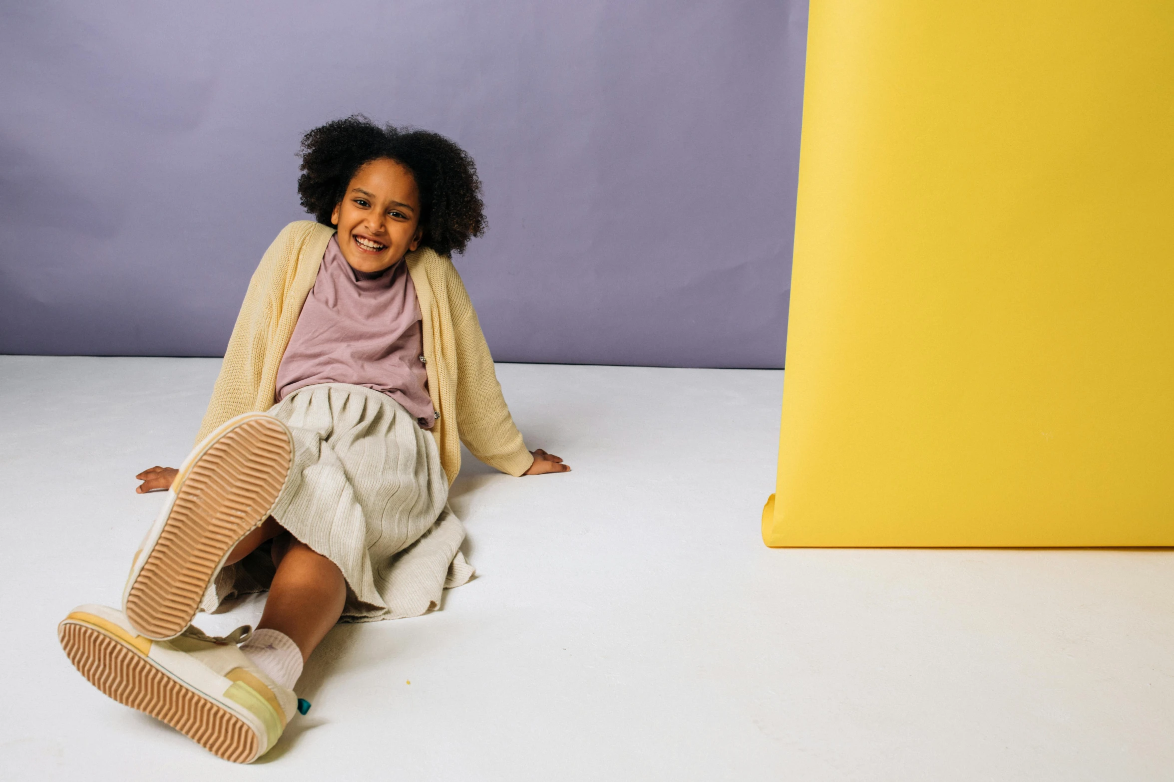 a smiling little girl wearing a sweater sitting on the ground