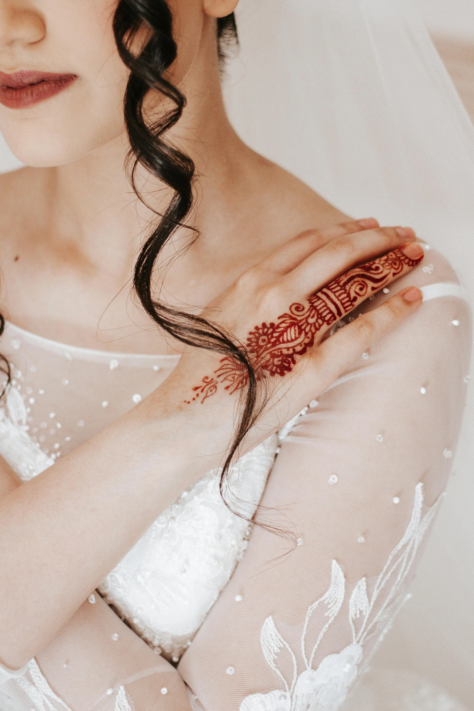 woman in veil looking down wearing red and white bridal jewelry