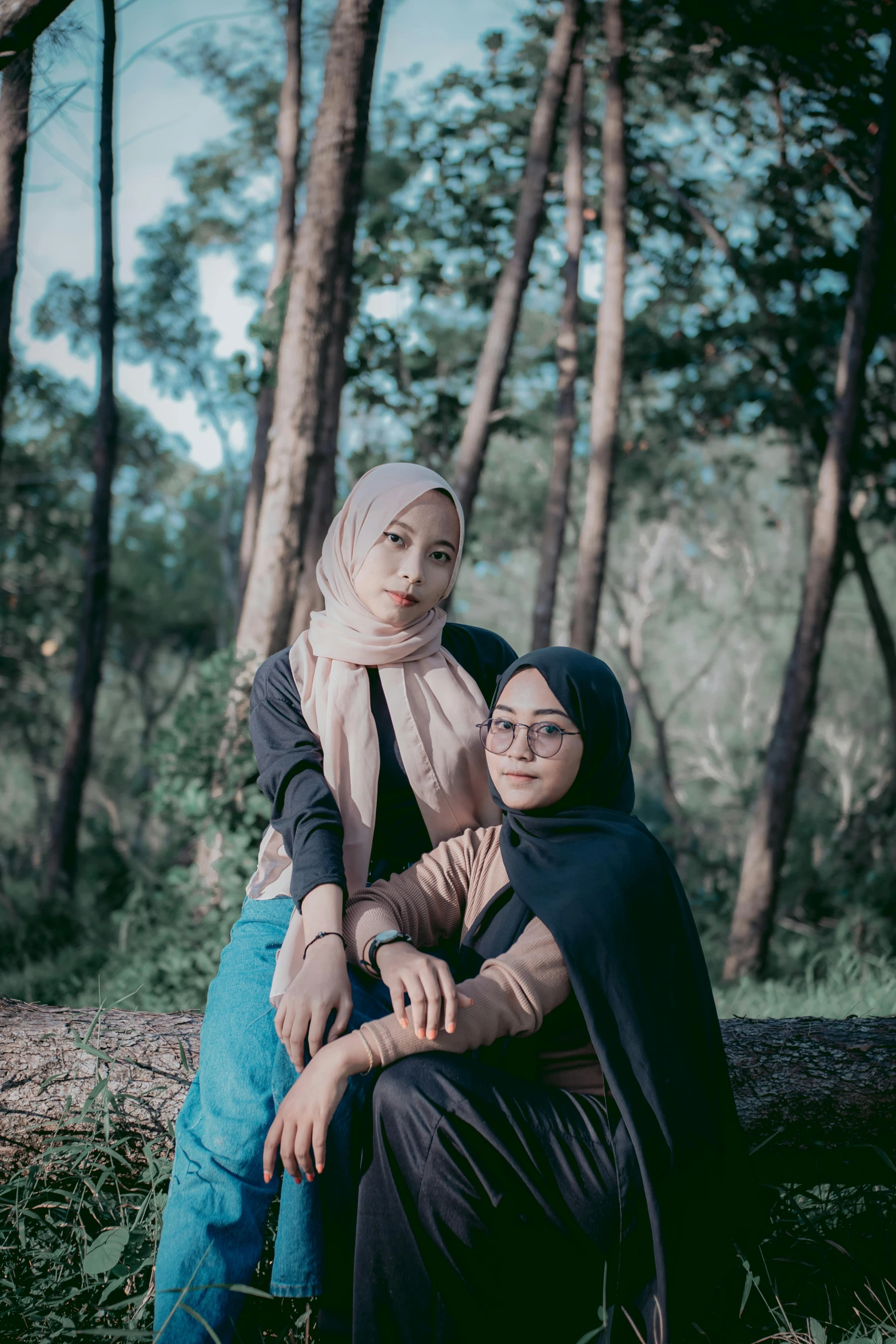 two women in headscarves sitting on a log outdoors