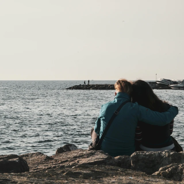 two people sitting on rocks by the water