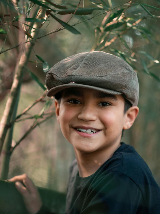 a boy wearing a hat stands by some trees