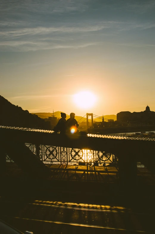 people sitting on top of an outdoor bridge as the sun sets