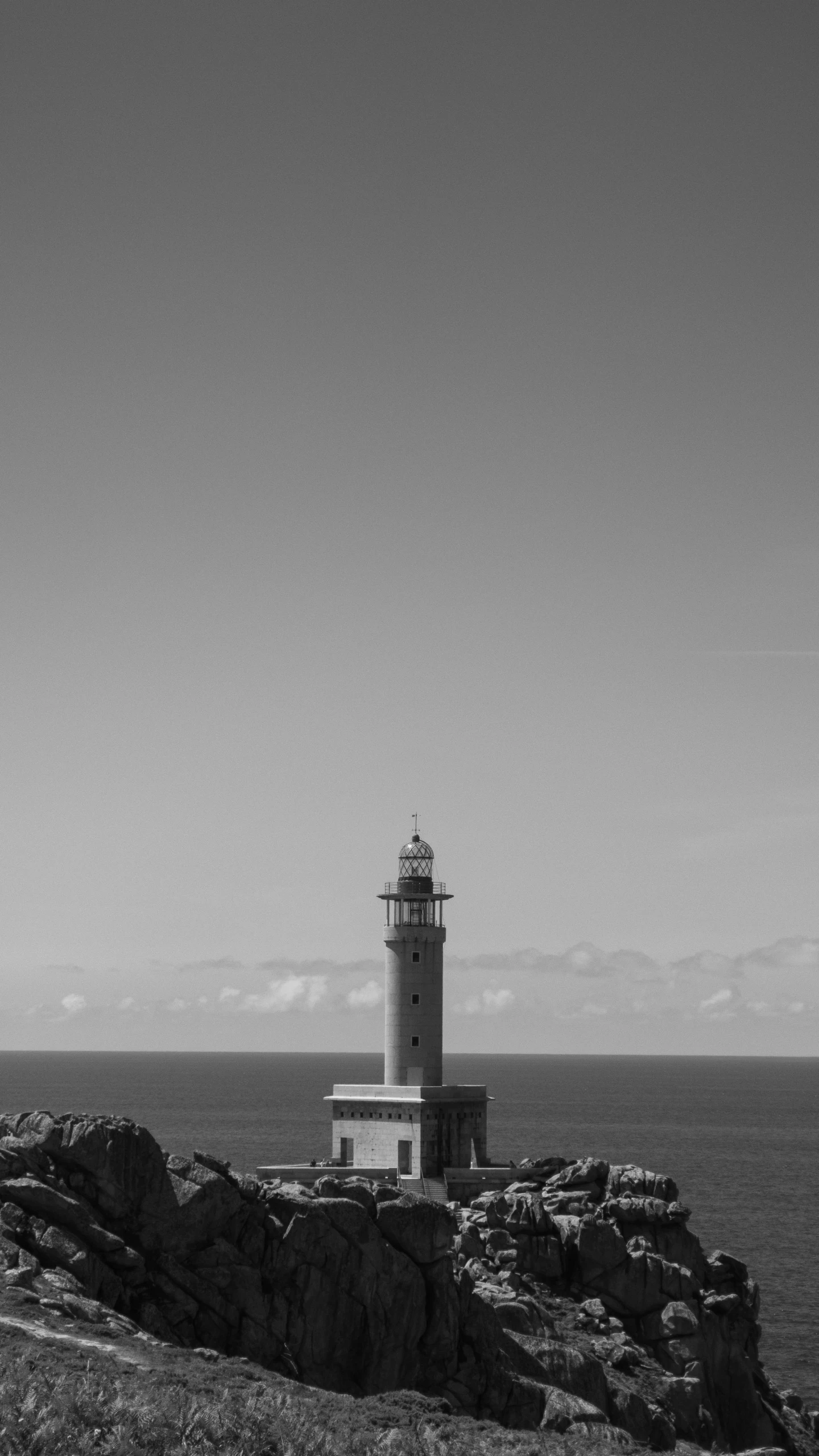 the light house sits on a cliff edge with a lighthouse and a small body of water in the distance