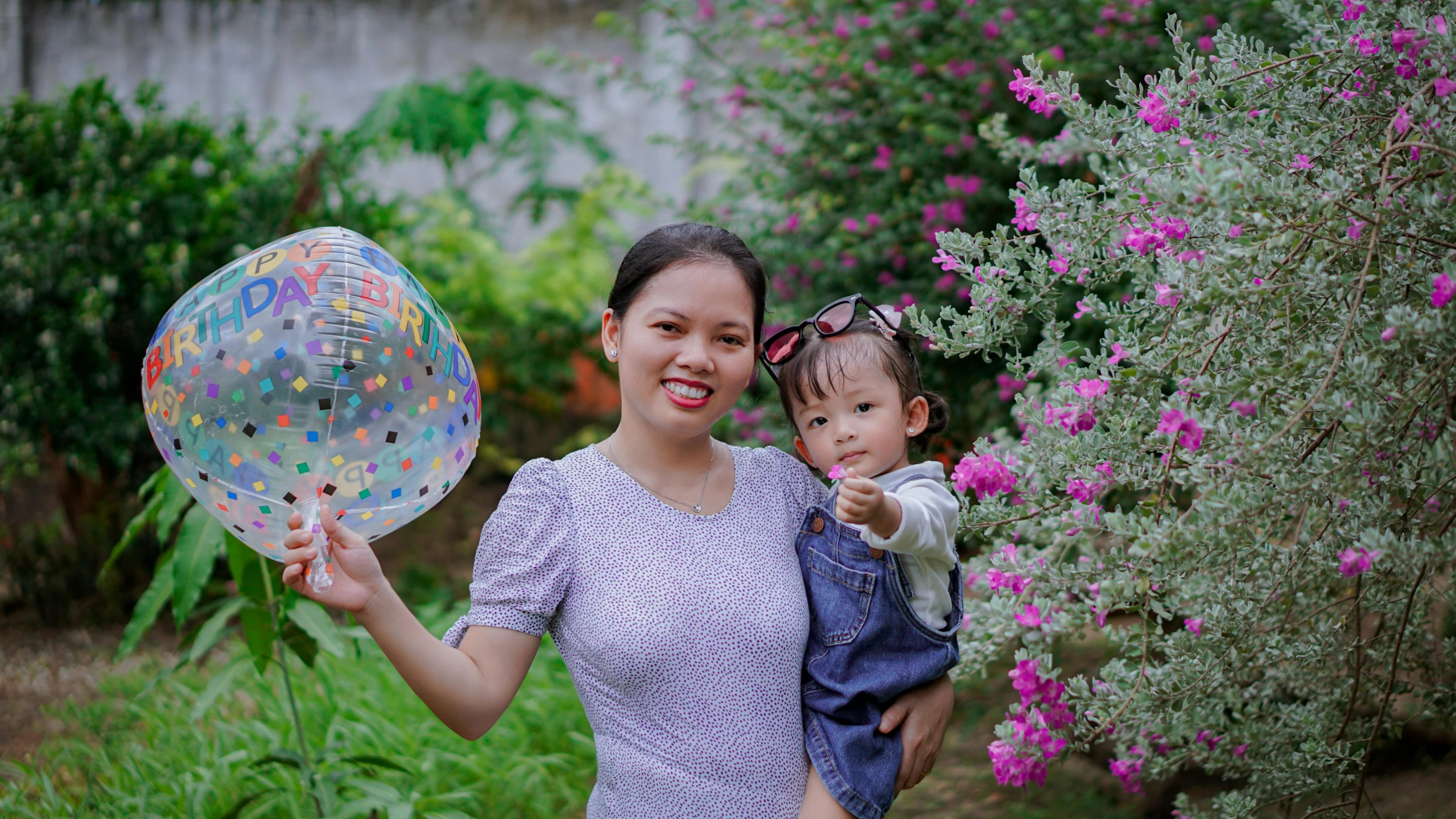 a mother holds her child in her arms and smiles as they hold up some decorative balloons