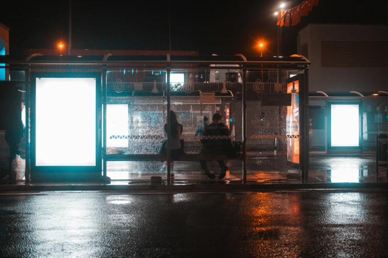 a bus stop at night with several people standing outside