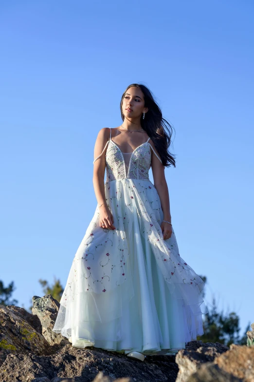 a woman is wearing a long dress standing on some rocks