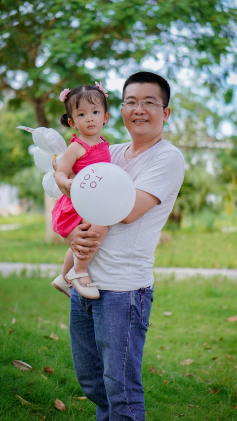 a man and girl holding white balloons in the park